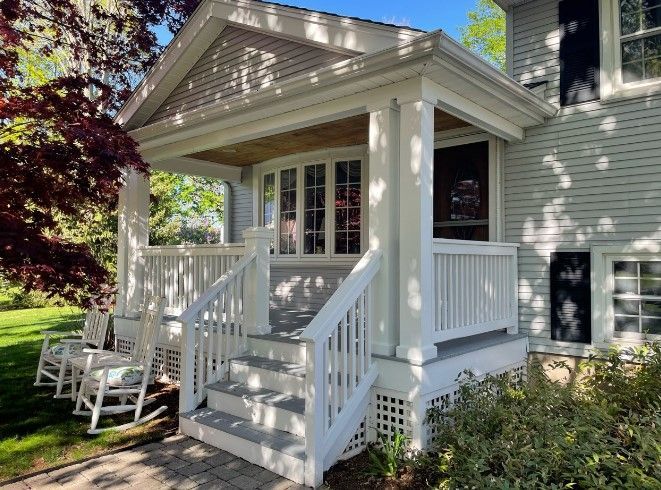 White-painted porch with steps on a gray house; rocking chairs visible; bright sunlight.