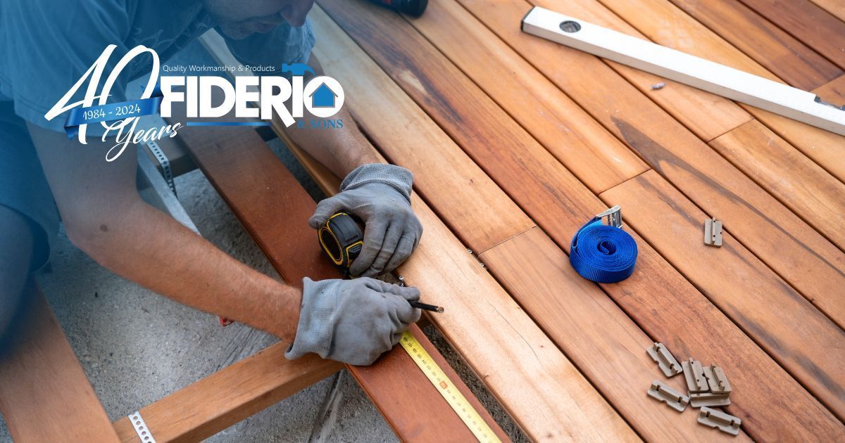Gloved hands measure wood planks with a tape measure; nails and tools lie on a workbench.