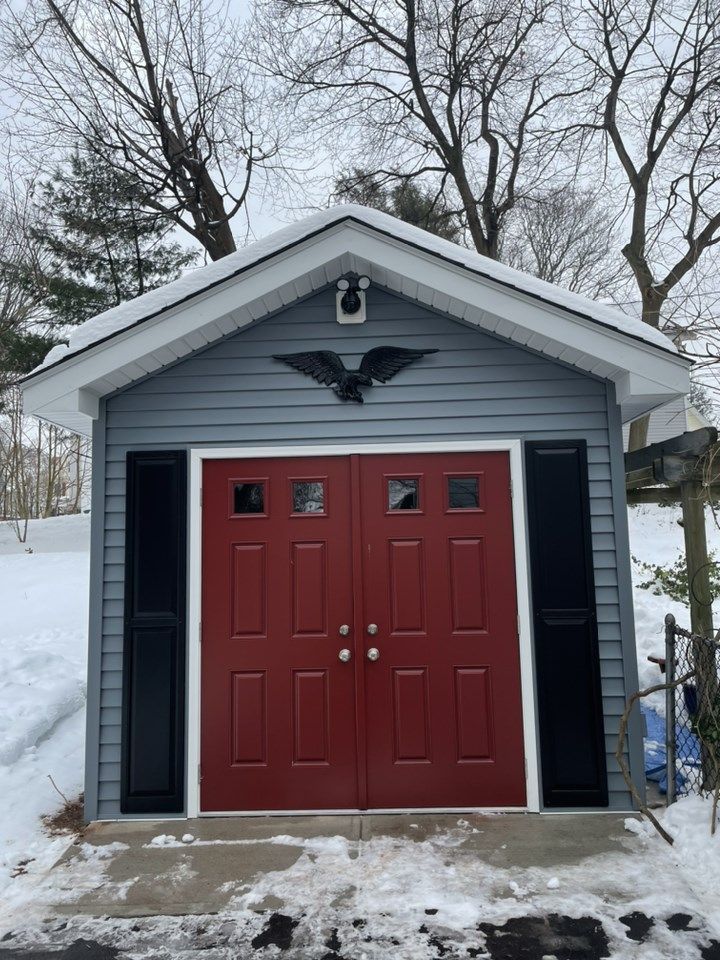 Small gray building with red doors, black shutters, and an eagle decoration in winter.