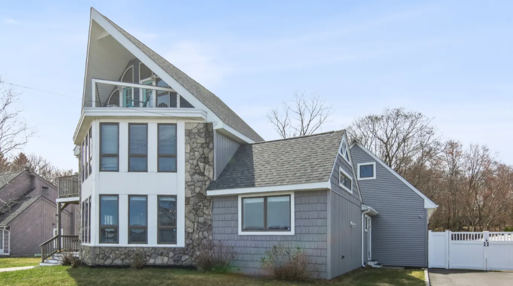 Two-story house with a unique angled roof and a small balcony. Gray and white exterior, blue sky backdrop.