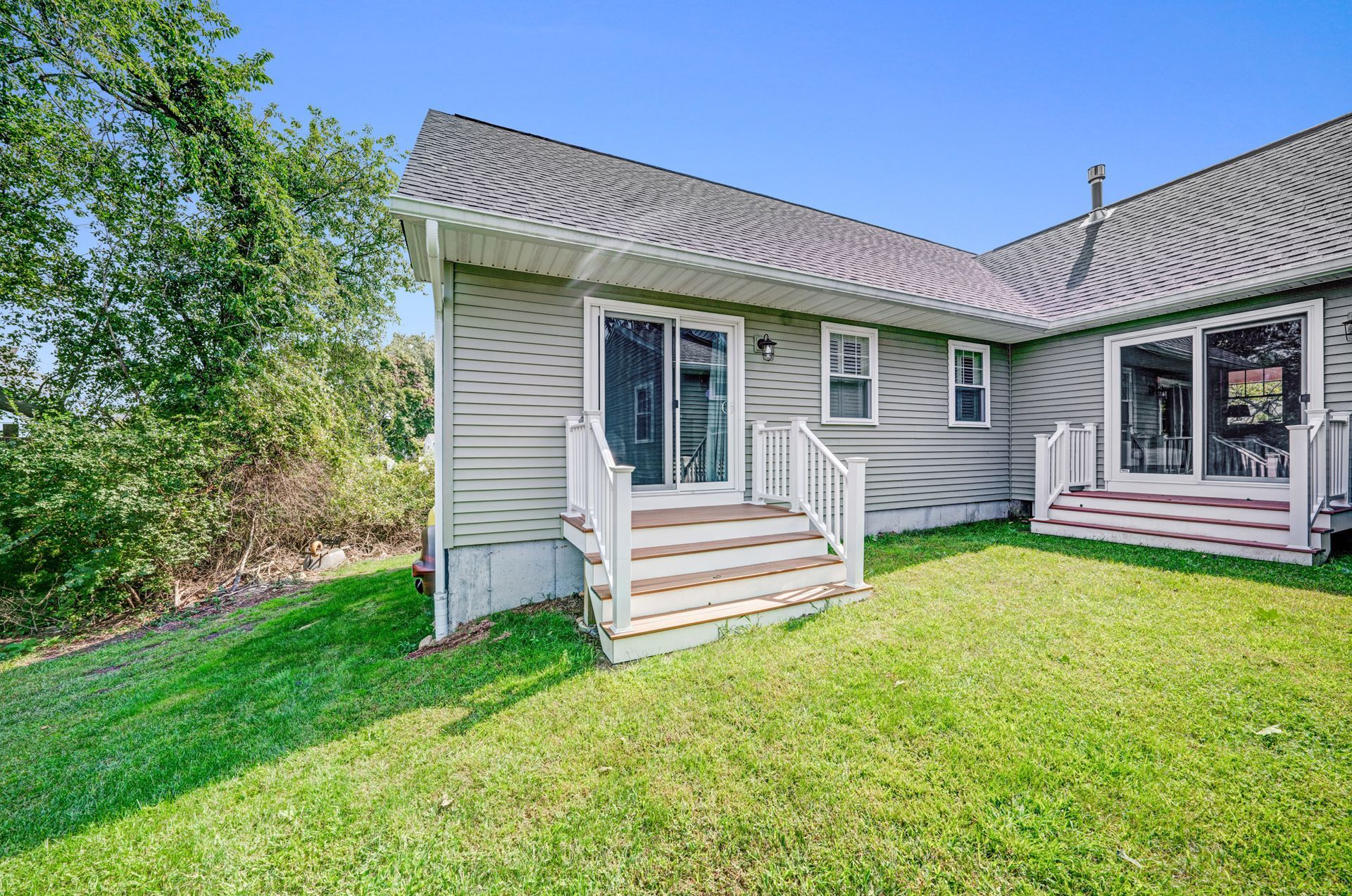Back exterior of a house with two sliding glass doors, wooden steps, and a grassy lawn under a blue sky.