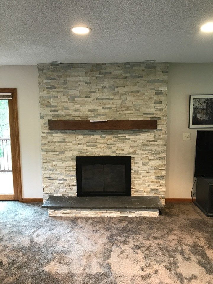 Stone-faced fireplace with dark hearth and wooden mantle in a room with gray carpet.
