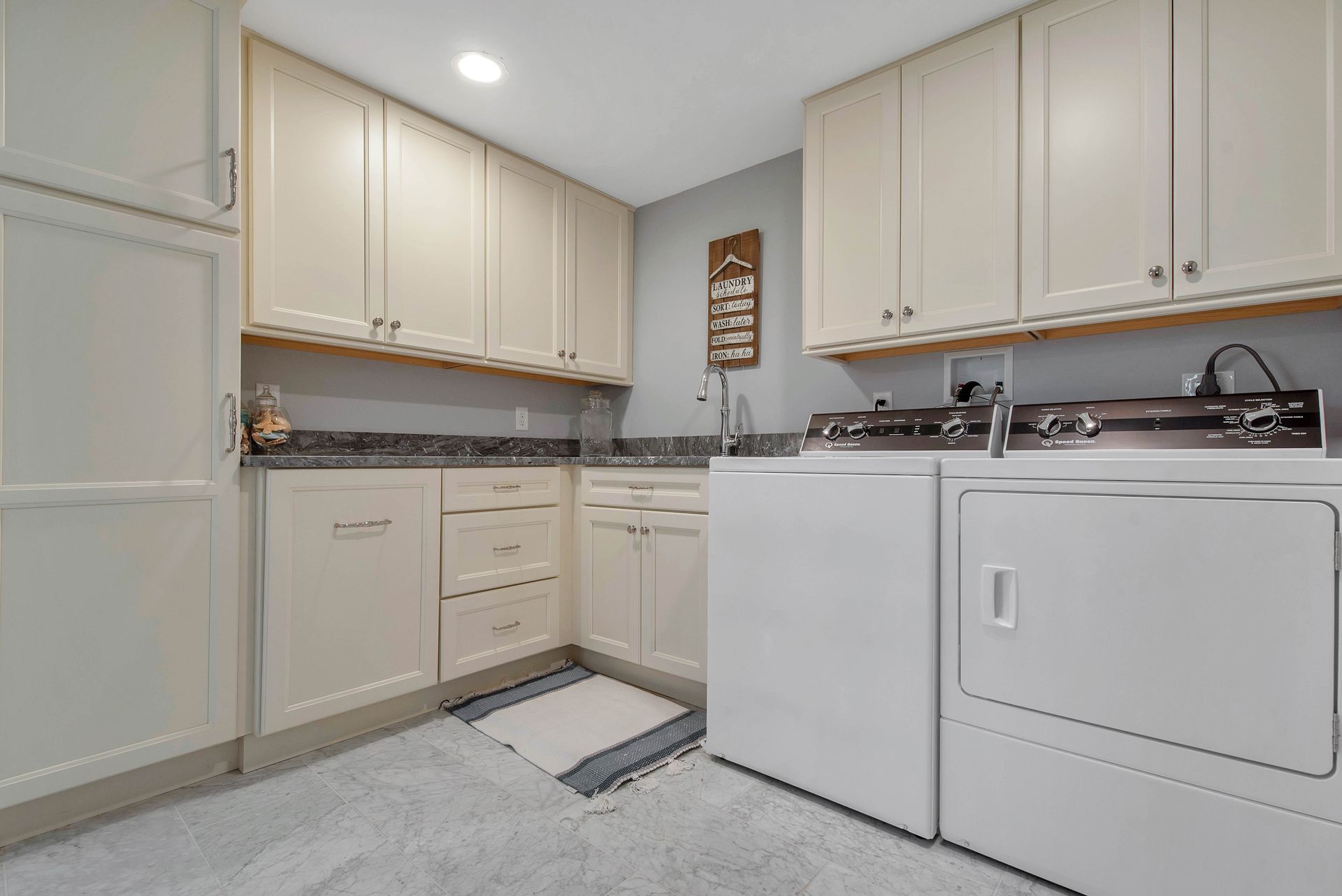 Laundry room with white cabinets, appliances, and gray countertop.