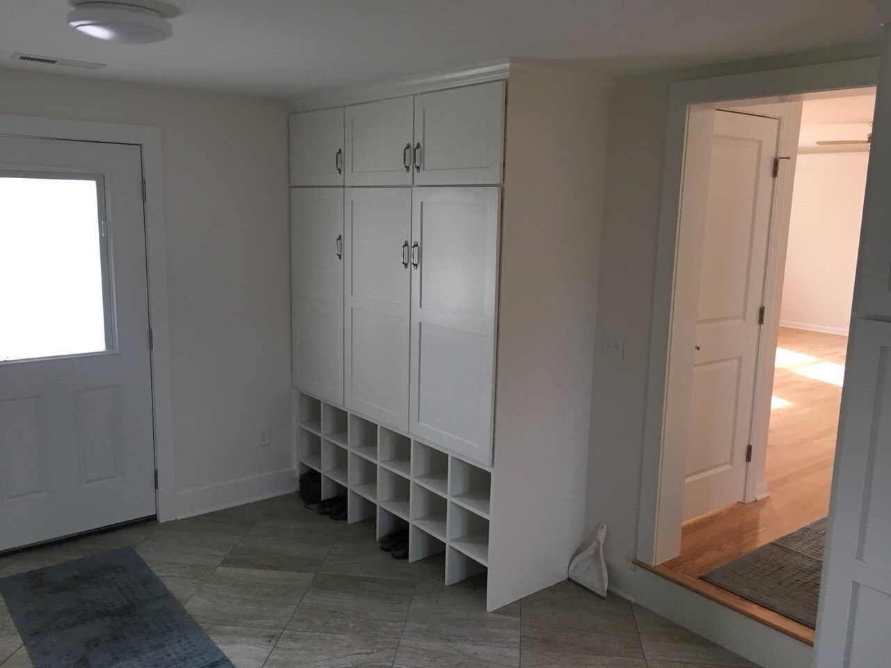 White cabinets with shoe cubbies in a room with a door and doorway to another room.