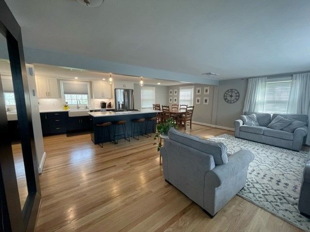 Open-concept kitchen and living room with blue island, wooden floor, gray furniture, and a rug.