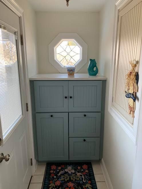 A narrow entryway with a teal cabinet, stained glass window, and patterned rug.