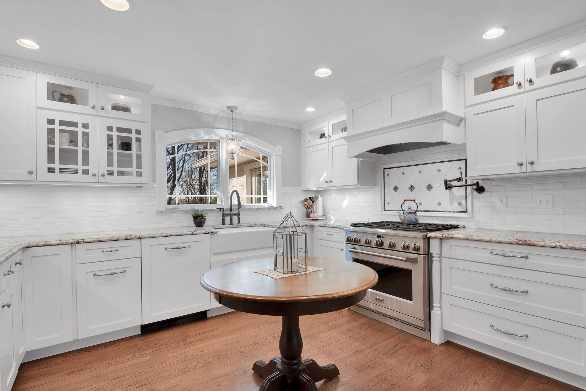 White kitchen with granite countertops, wooden floor, and a round wooden table.