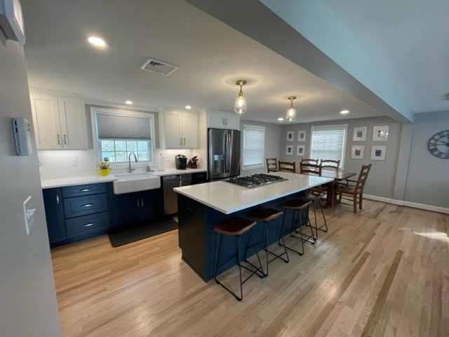 Modern kitchen with blue and white cabinets, island with stovetop, dining table, and wood floors.