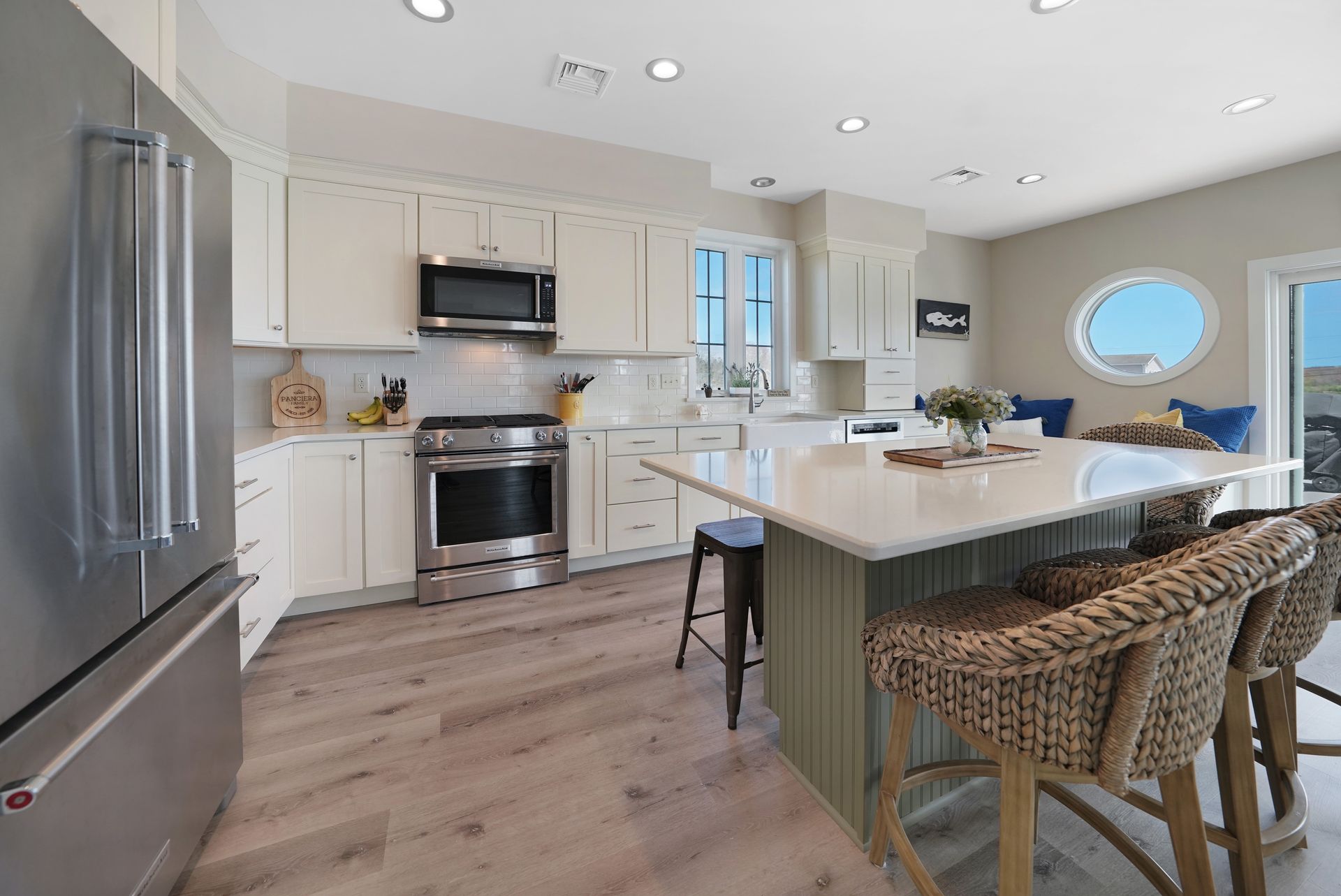 Kitchen with white cabinets, stainless steel appliances, island with stools, and light wood floors.