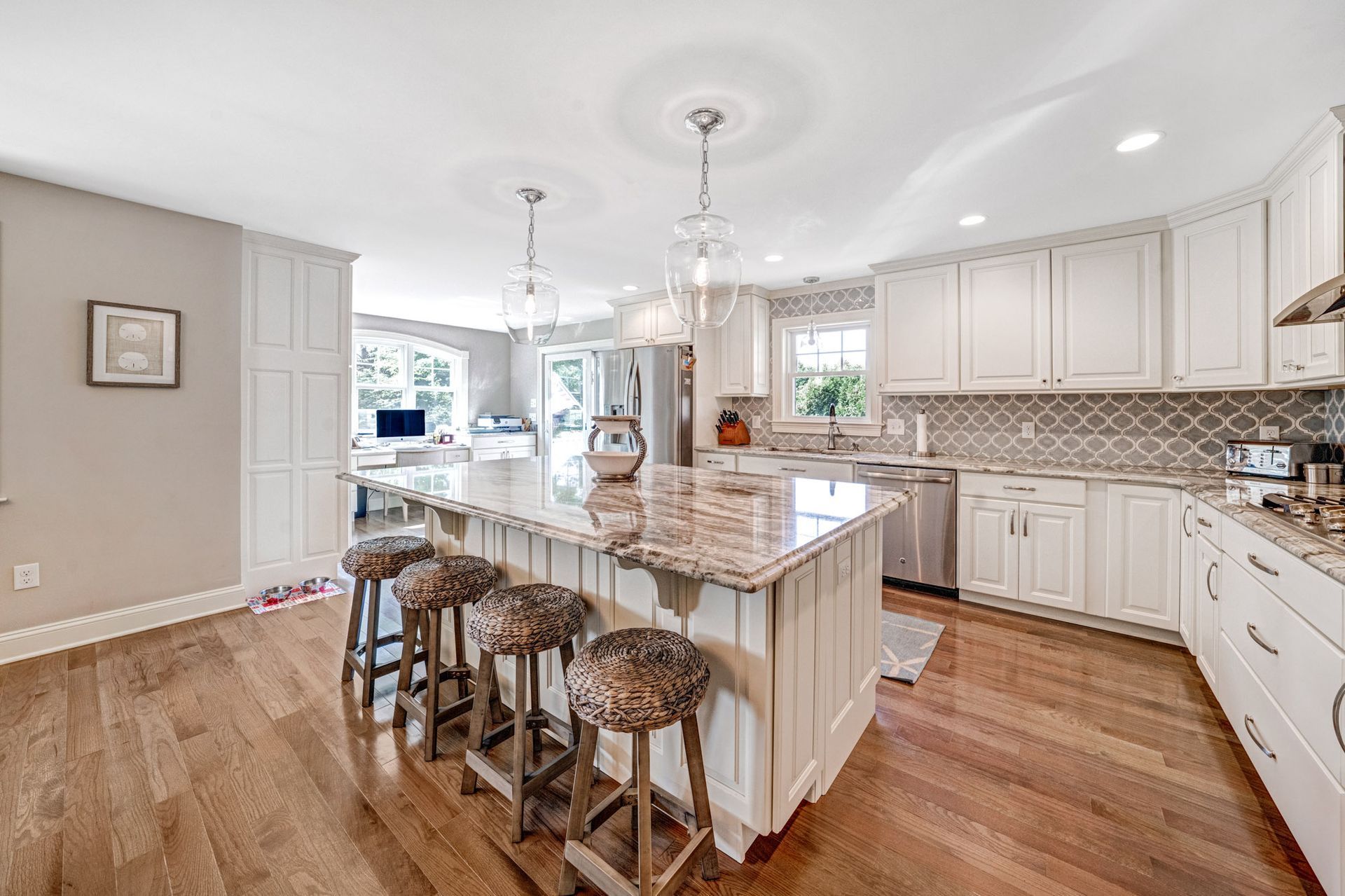 Spacious kitchen with a large island, white cabinets, and wooden floors.  Bar stools sit at the island.