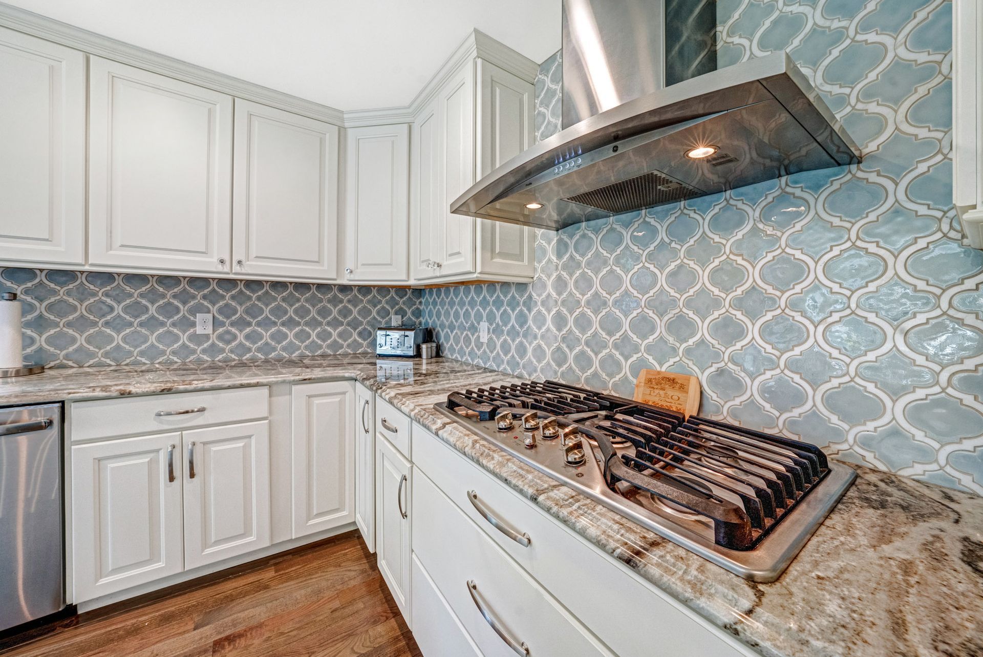 White kitchen cabinets with blue patterned backsplash, stainless steel range and hood.