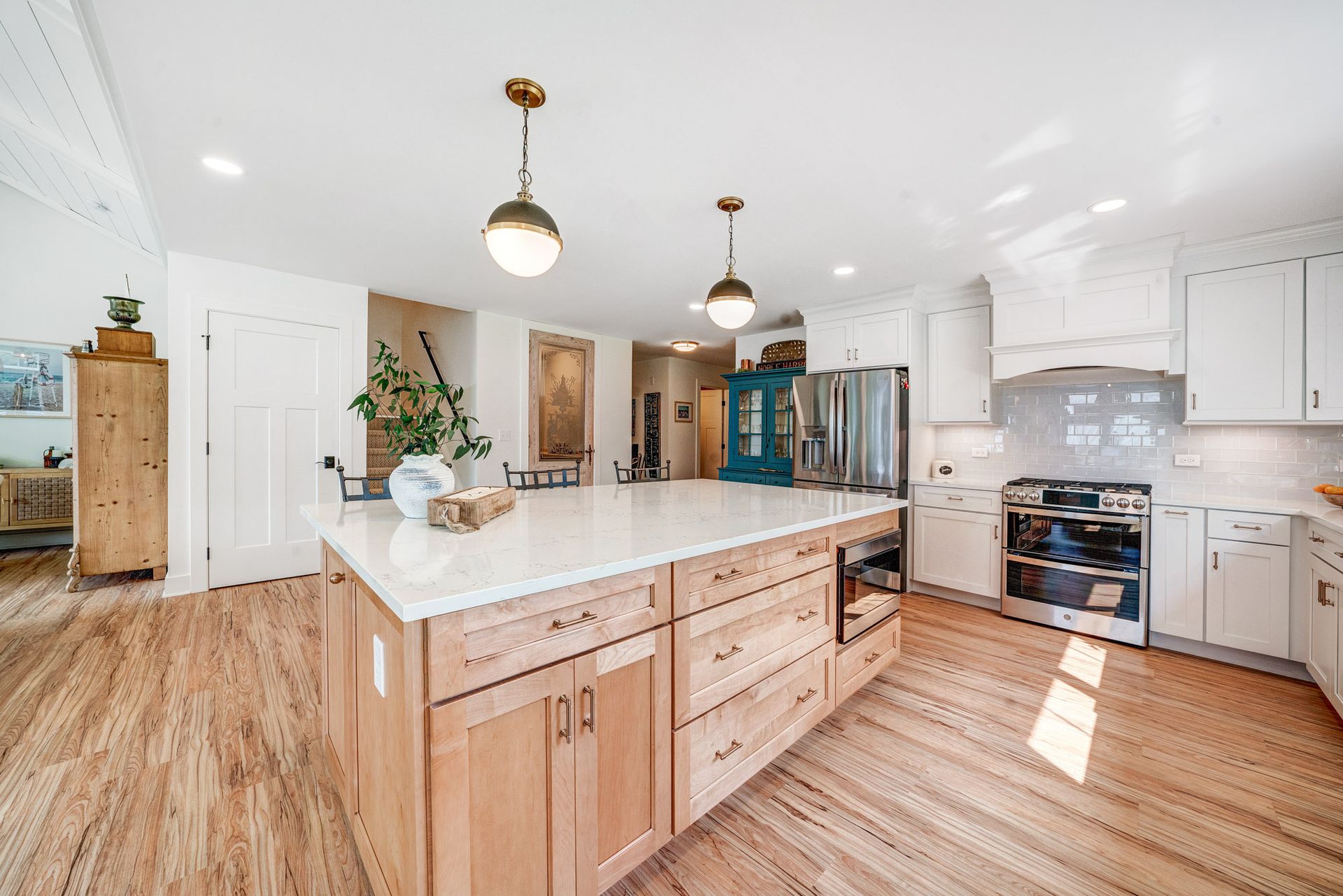 Bright kitchen with large island, light wood cabinets, and white countertops. Two pendant lights hang overhead.