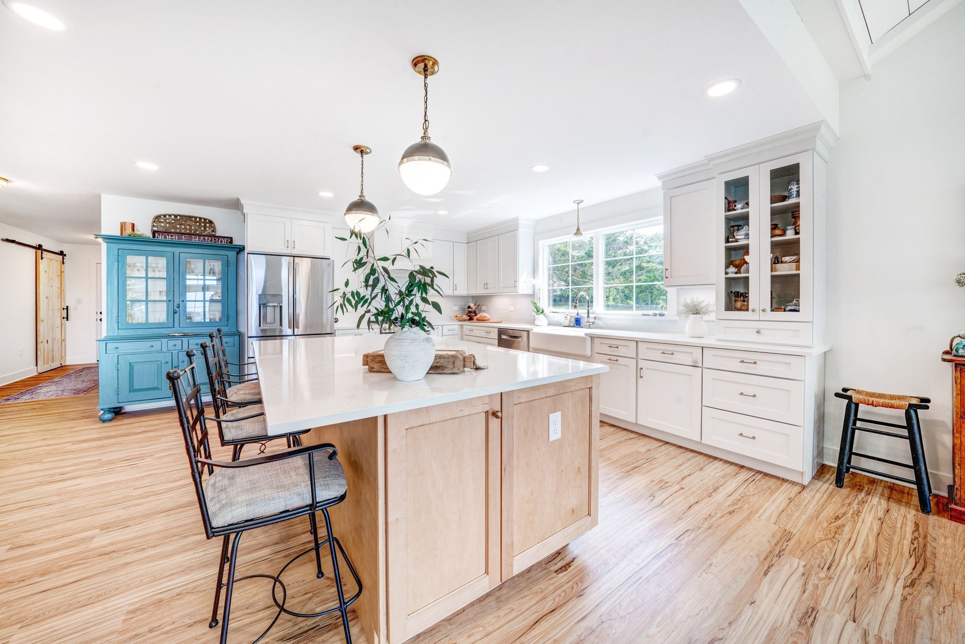 Spacious, bright kitchen with a large island, white cabinets, and wooden floors.