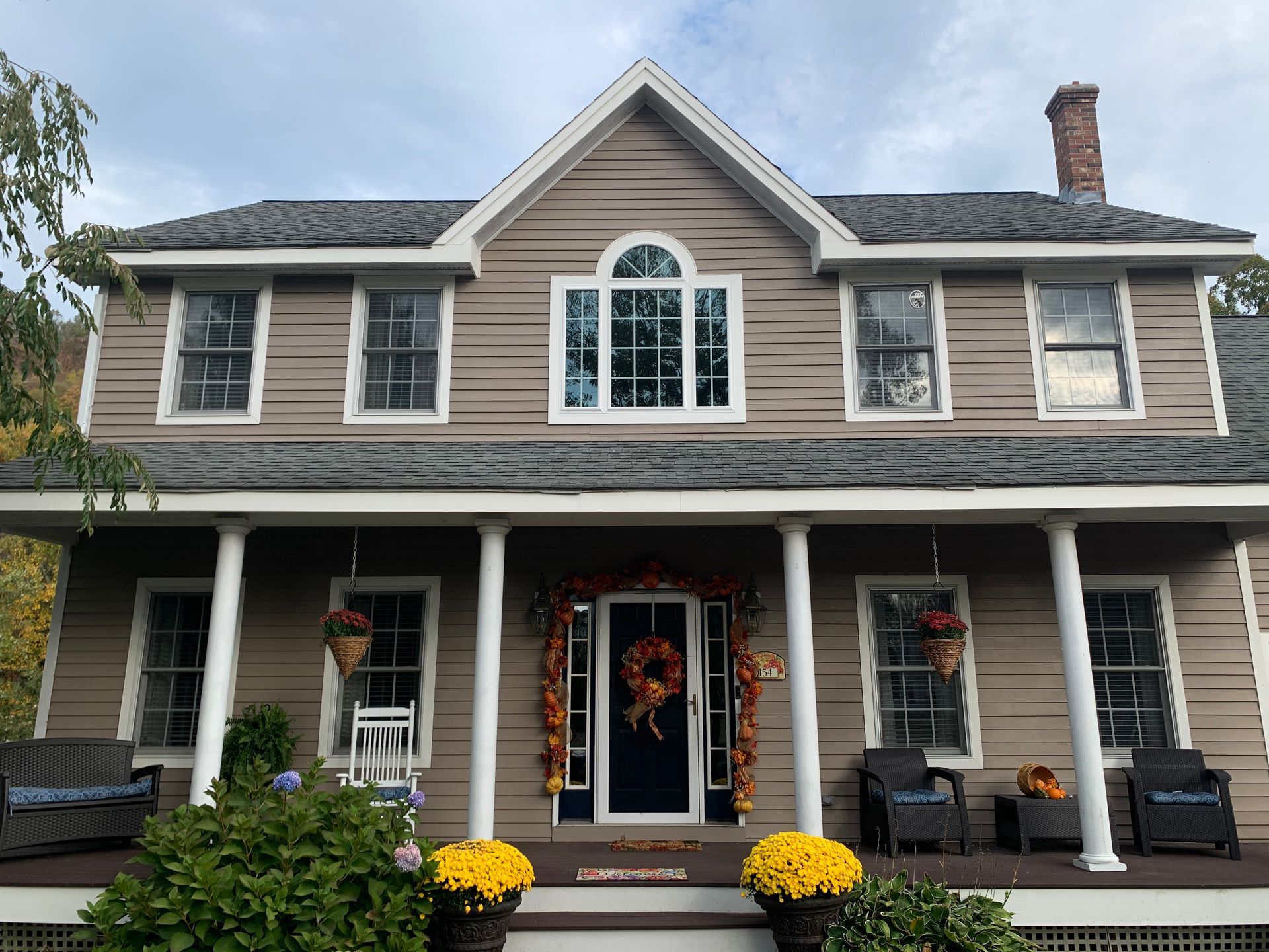 Two-story brown house with a porch decorated for fall.