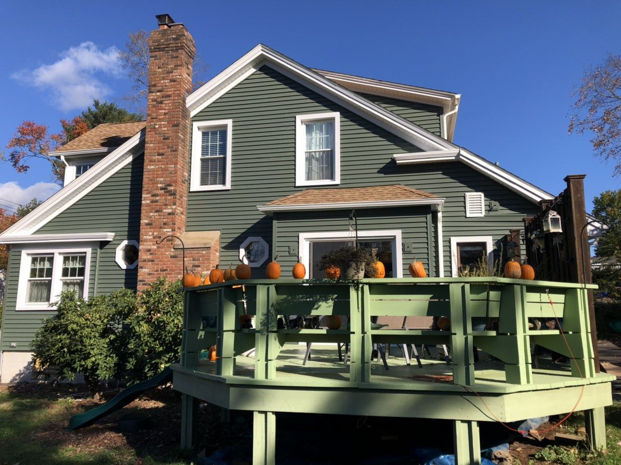 Green house with a deck lined with pumpkins, under a clear, blue sky.