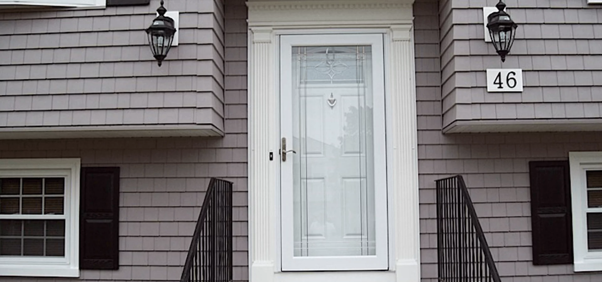 Front door of a house with gray siding. Black railings and shutters. Address 46 on the wall.