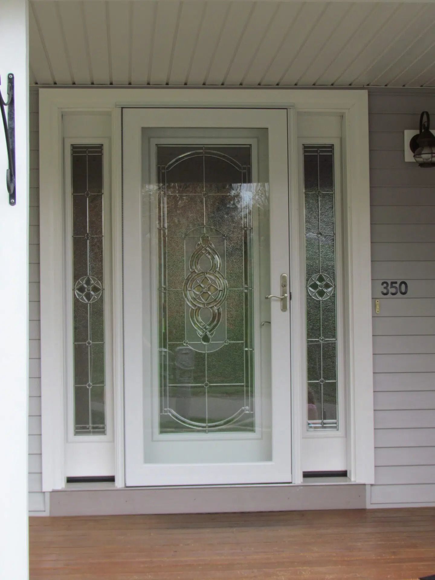 White glass-paneled front door with sidelights, set in a white frame, with a gray house exterior.