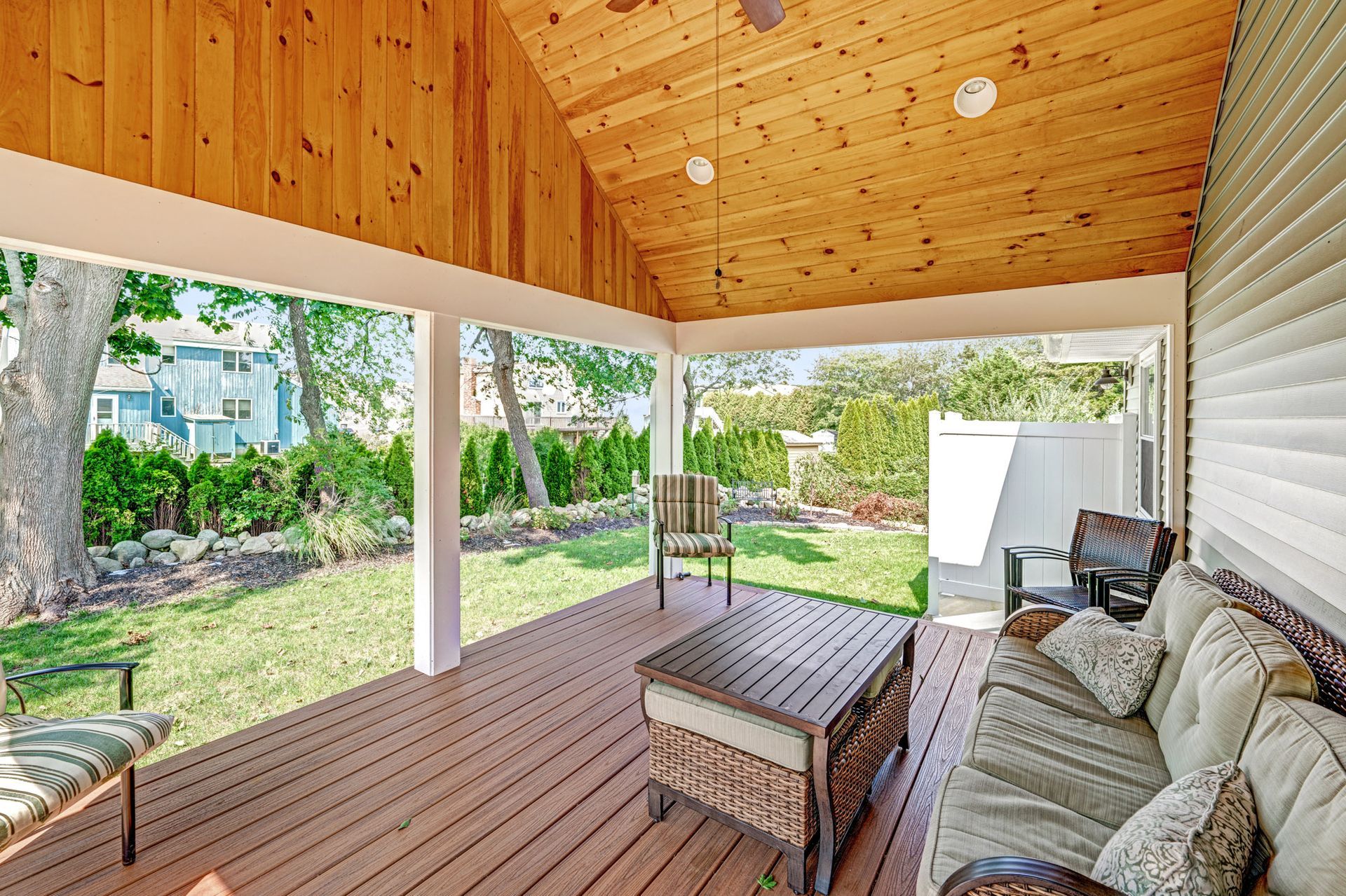 Covered outdoor patio with wood ceiling, seating, and view of a yard.
