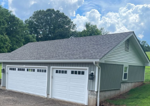 Two-car garage with gray roof, white garage doors, and green siding under a cloudy sky.