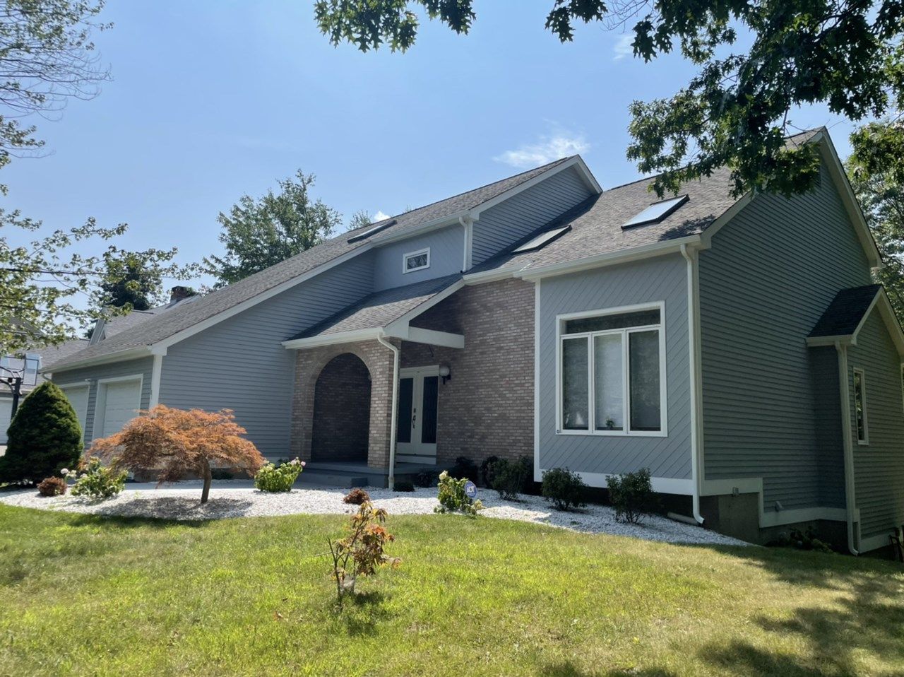House with gray siding and roof, brick entrance, and windows, set on a green lawn.
