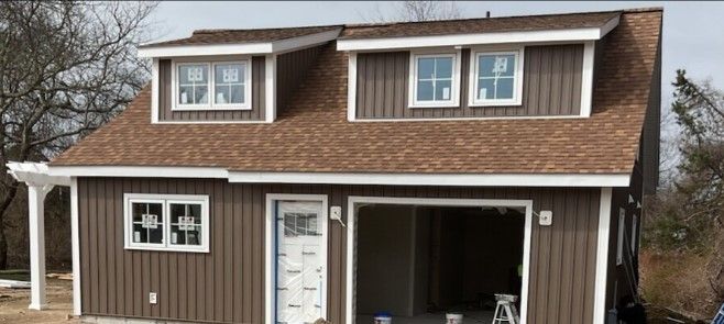 Brown two-story building with garage door, windows, and dormers under construction.