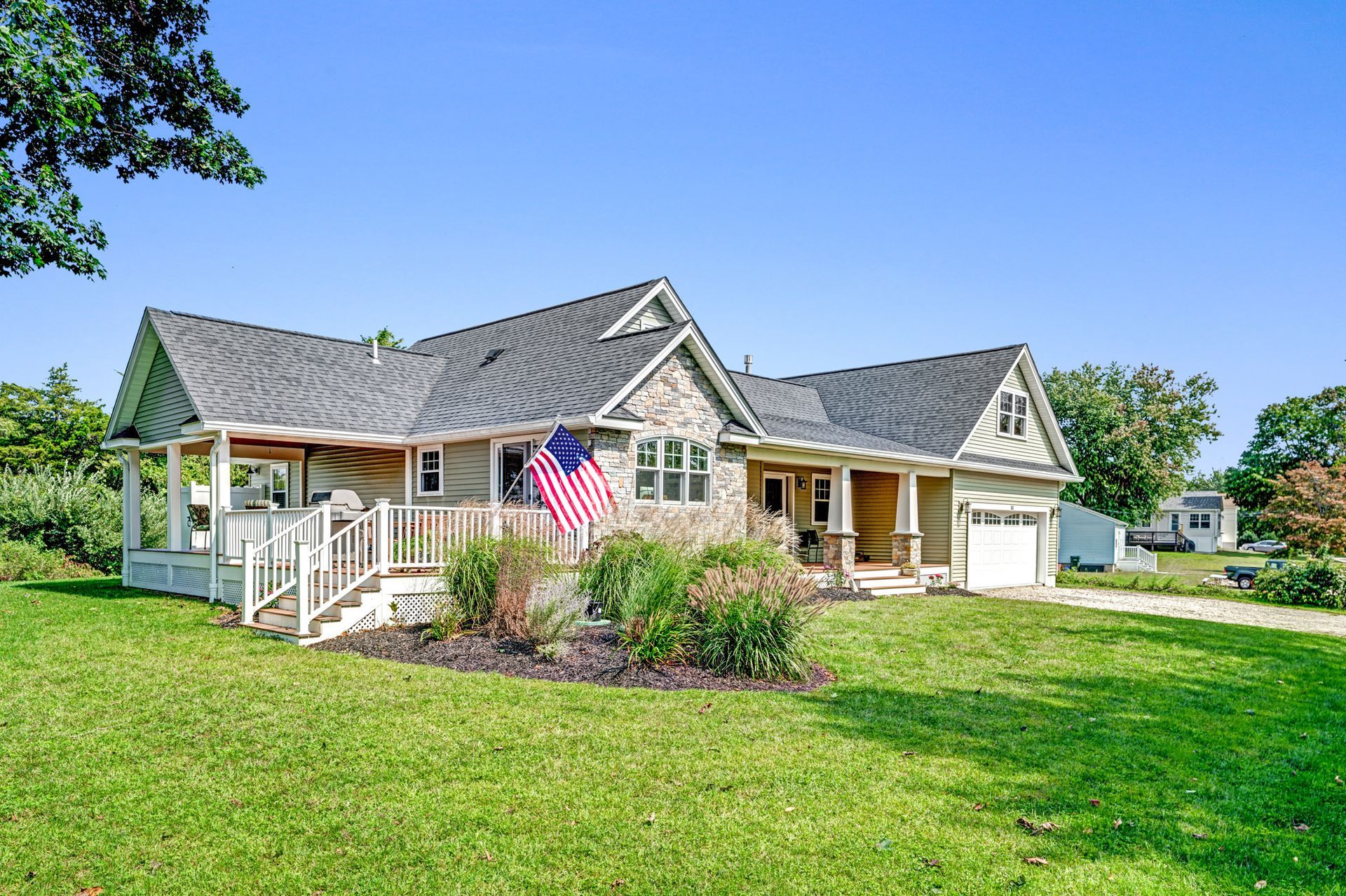 Bungalow house with covered porch, American flag, green lawn, and blue sky.