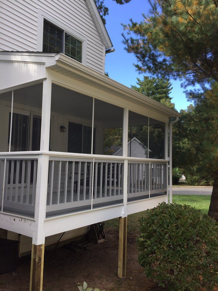 Screened-in porch attached to a white house with a deck. The porch has a white railing, roof, and screens.