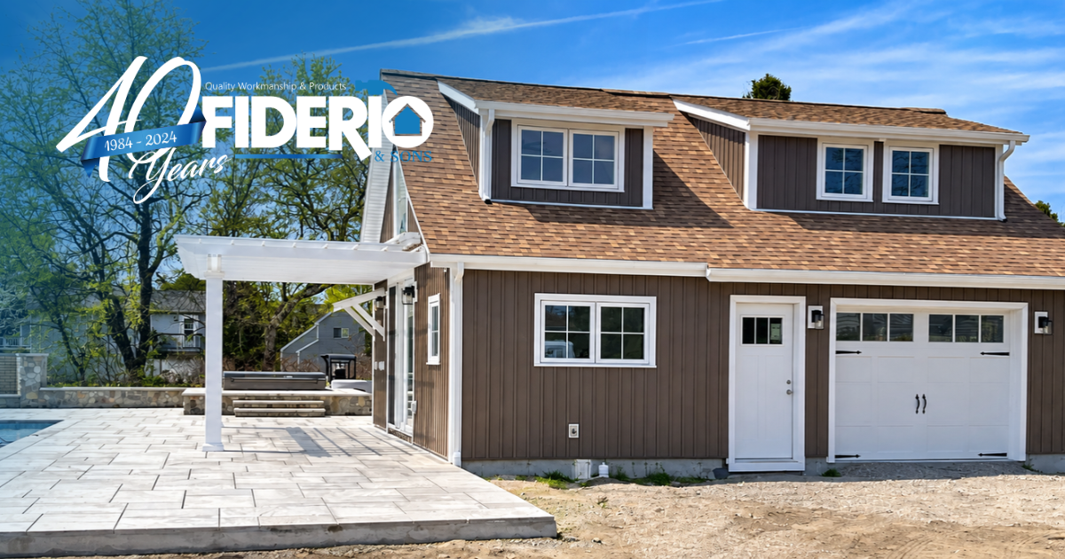 Modern two-story brown house with white trim and garage, next to a covered patio and deck under blue sky
