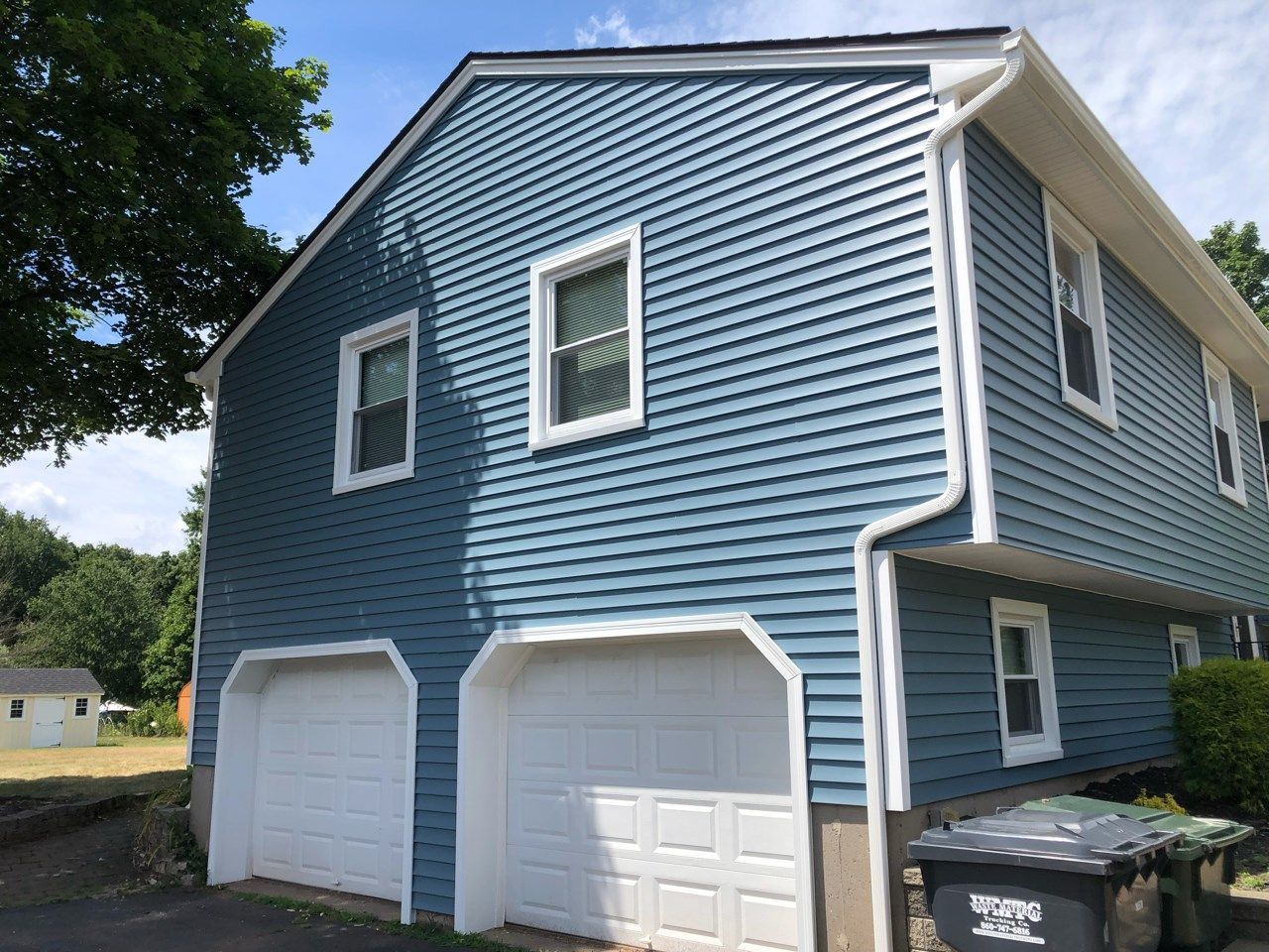 Blue-sided two-story house with white trim, two garage doors, and windows.