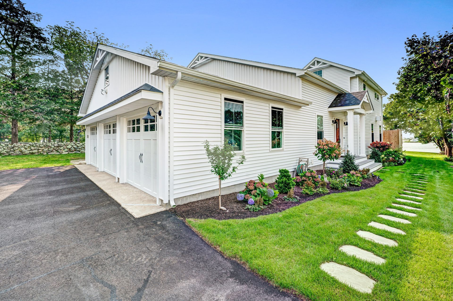 White house with attached three-car garage, black asphalt driveway, and green lawn with stepping stones.
