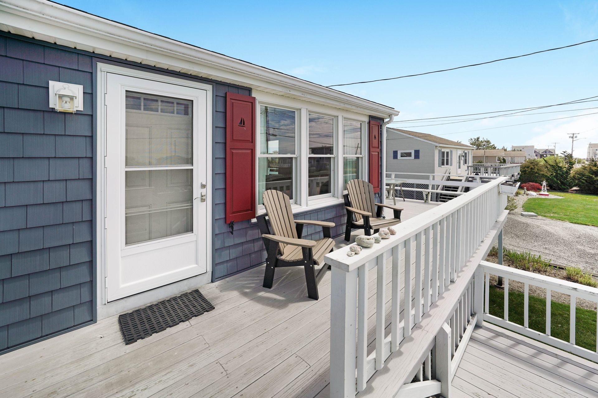 A blue shingled beach house with a white porch and red shutters; two chairs are on the porch.