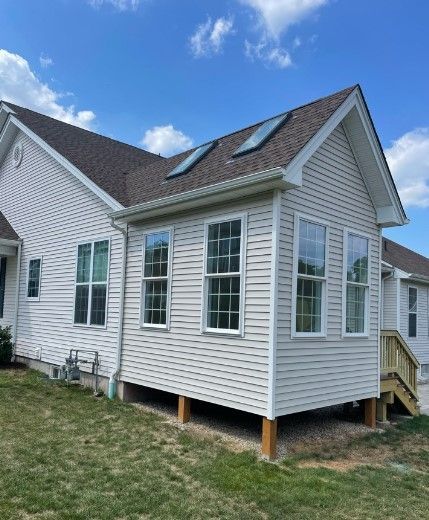 Beige house with a new sunroom addition, windows, and skylights under a blue sky.
