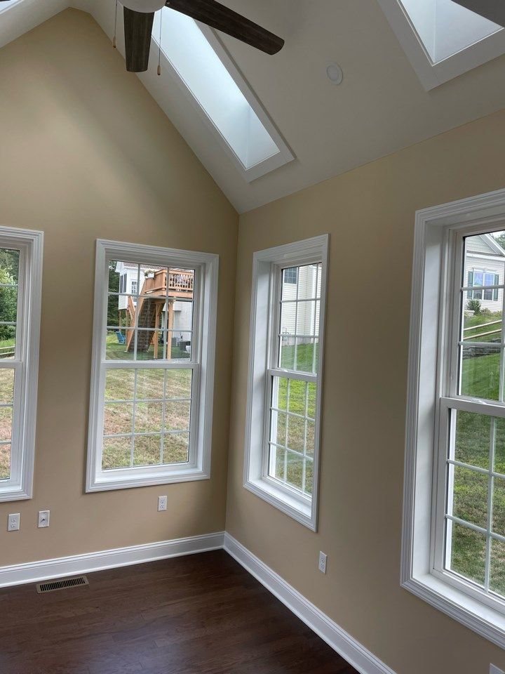 Interior room with windows, skylights, and ceiling fan. Light tan walls, white trim, and dark wood floor.