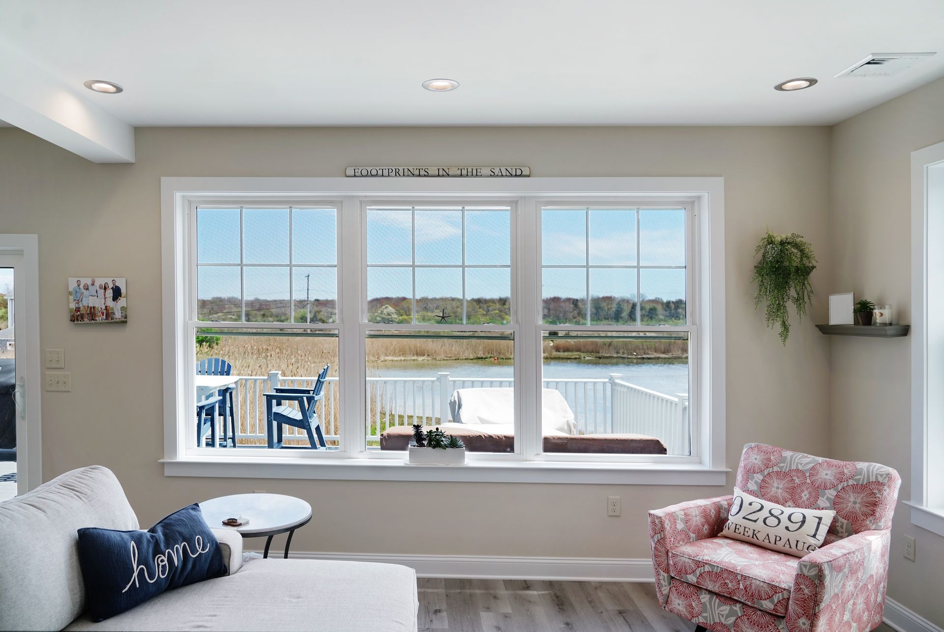 Living room with large windows overlooking a waterfront. A couch, floral armchair, and small table are in the room.