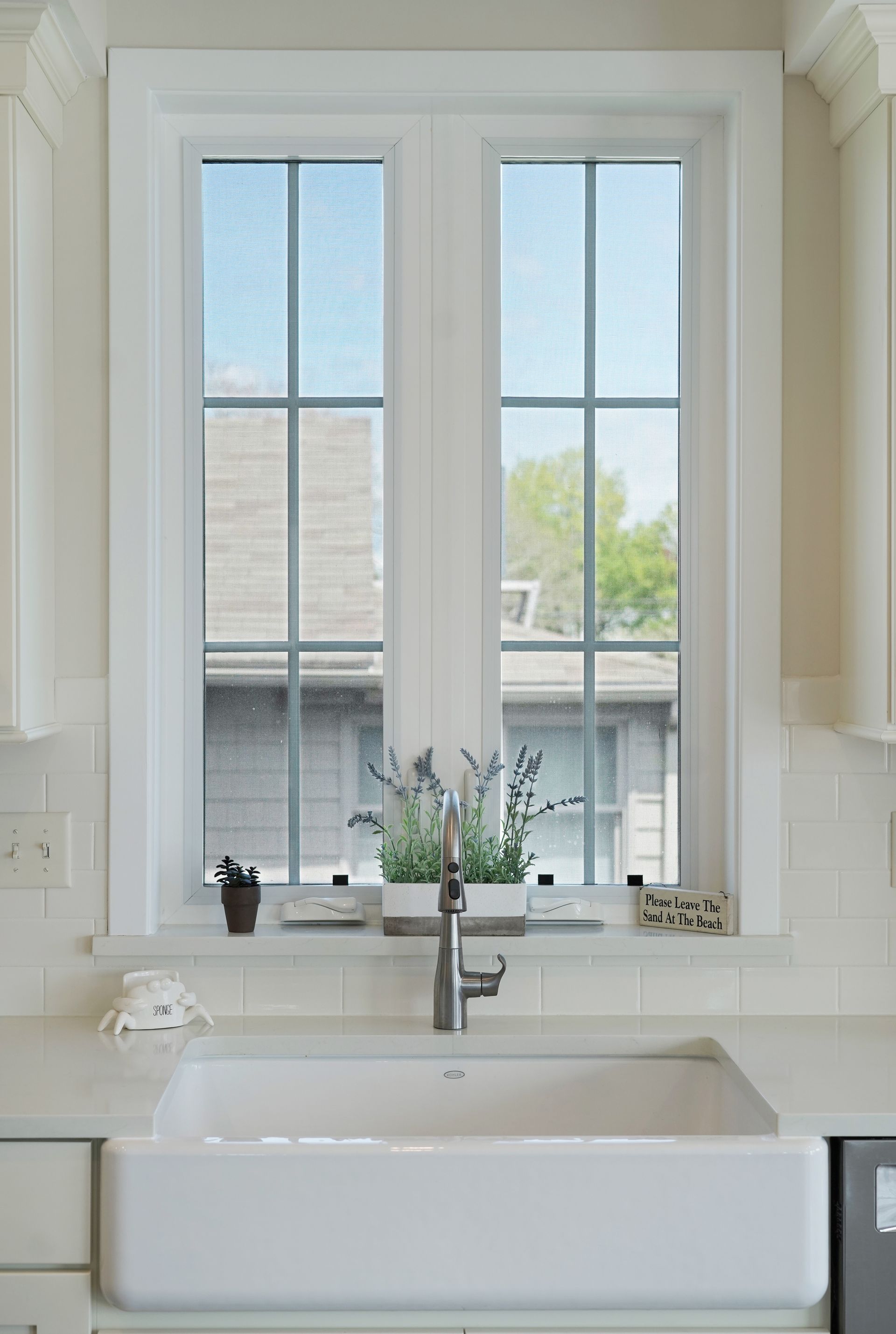 Kitchen sink beneath a window with grid pattern. Lavender and potted plant sit on the windowsill.