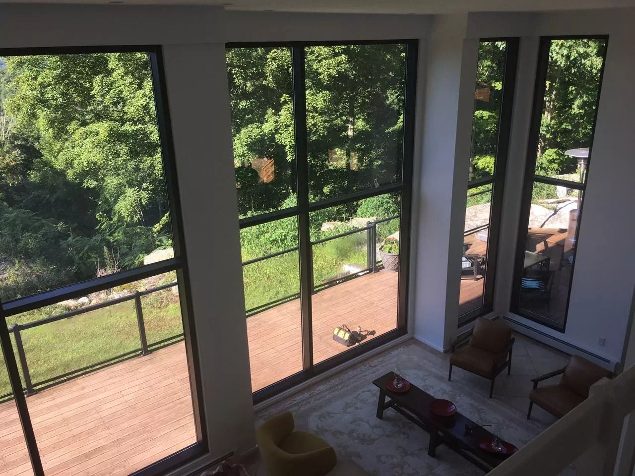 High-angle view of a room with large windows overlooking a deck and lush green trees.