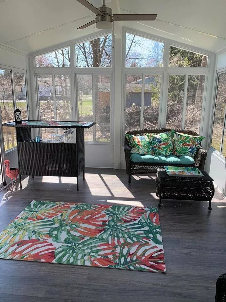 Sunroom with a bar, wicker furniture, colorful rug, and large windows.