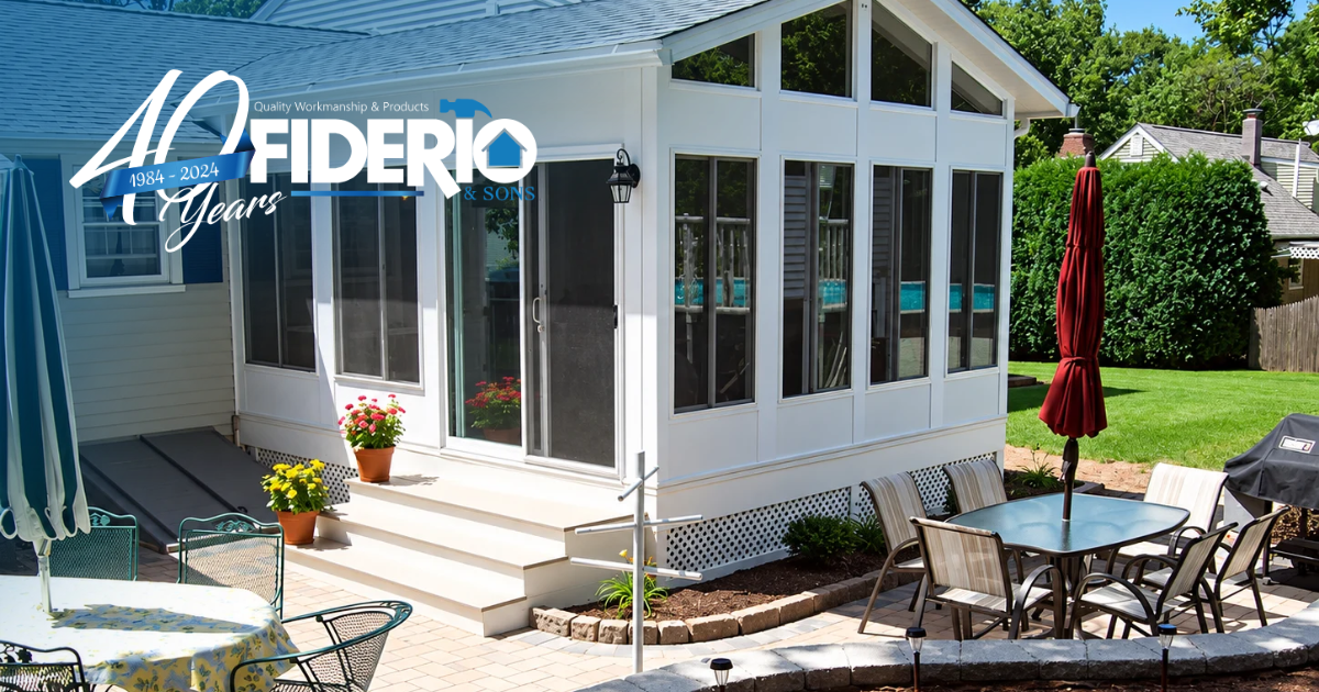 Bright sunroom with wicker seating, pink cushions, white walls, and large windows opening to a backyard.