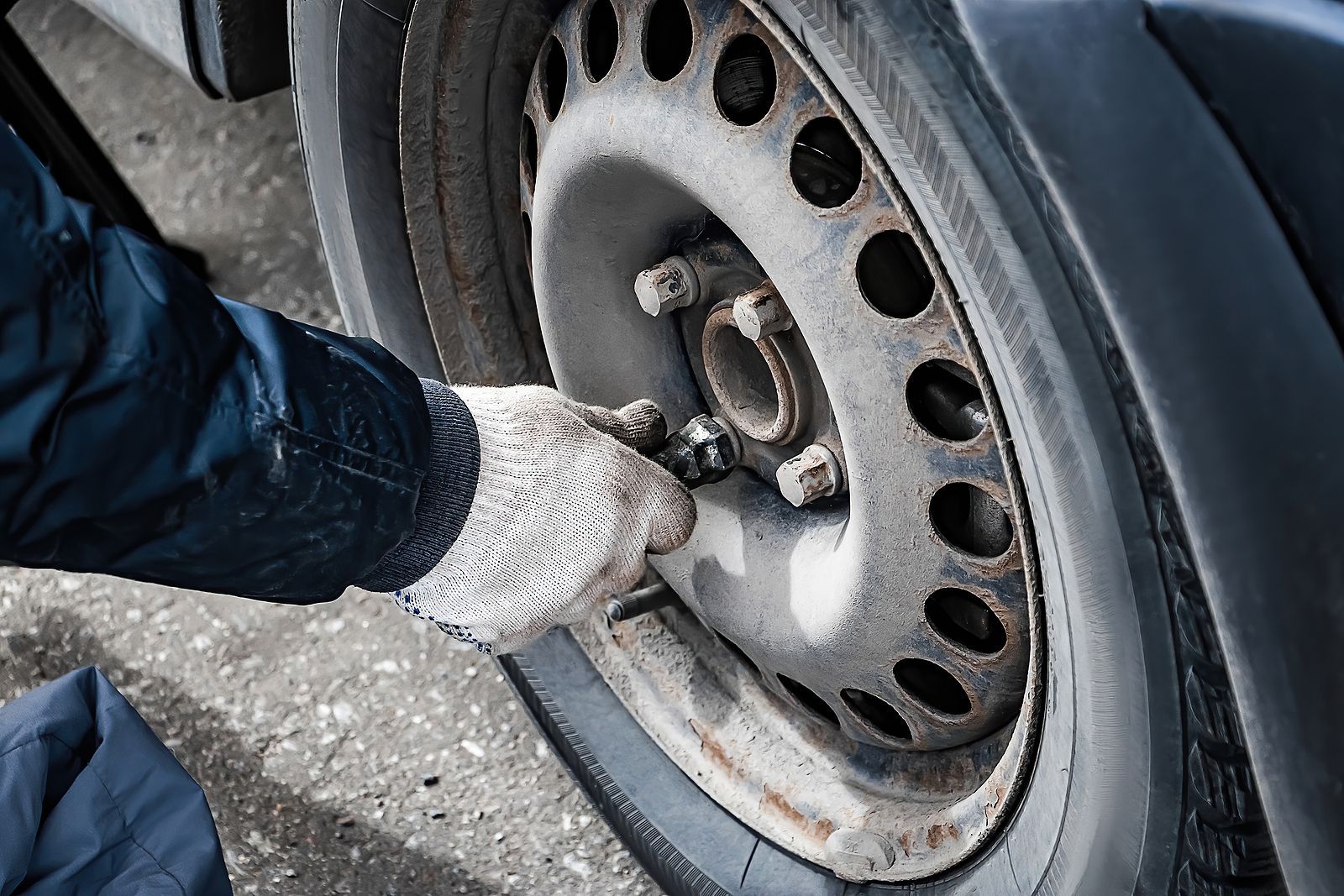 A person is changing a tire on a car with a wrench.