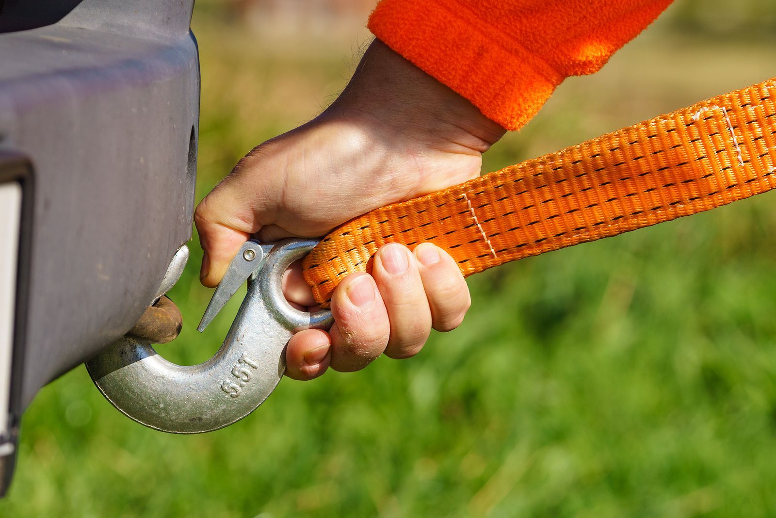 A person is holding a tow strap attached to the back of a car.