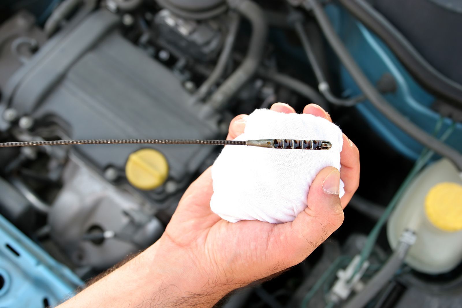 A person is holding a dipstick in front of a car engine