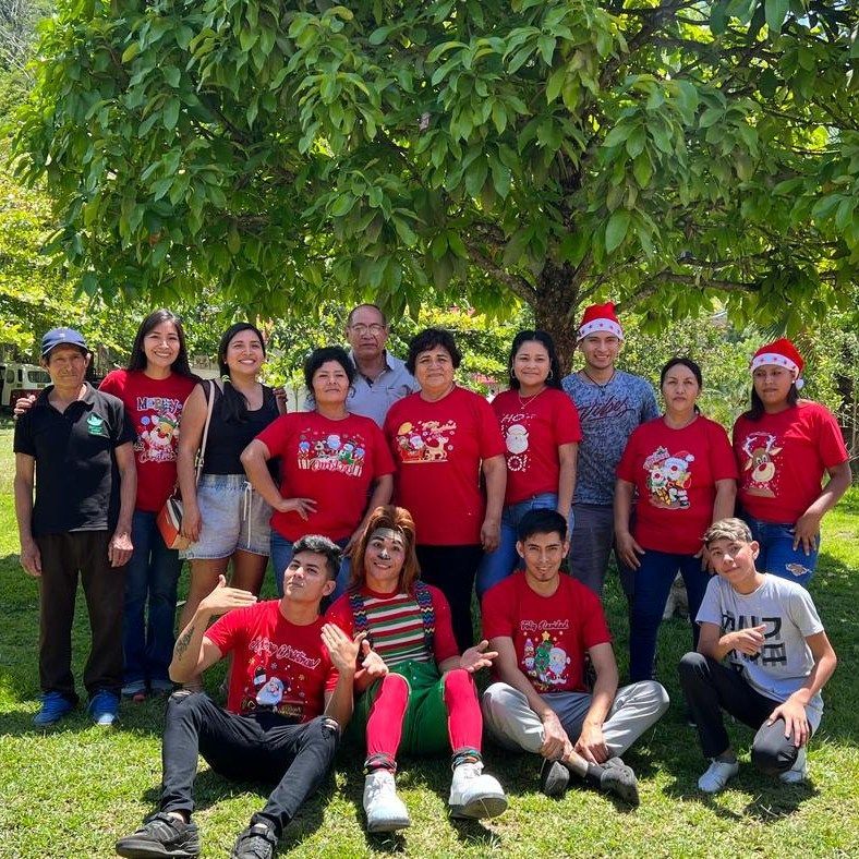 Grupo de personas con camisetas rojas posando juntas al aire libre bajo un árbol frondoso.
