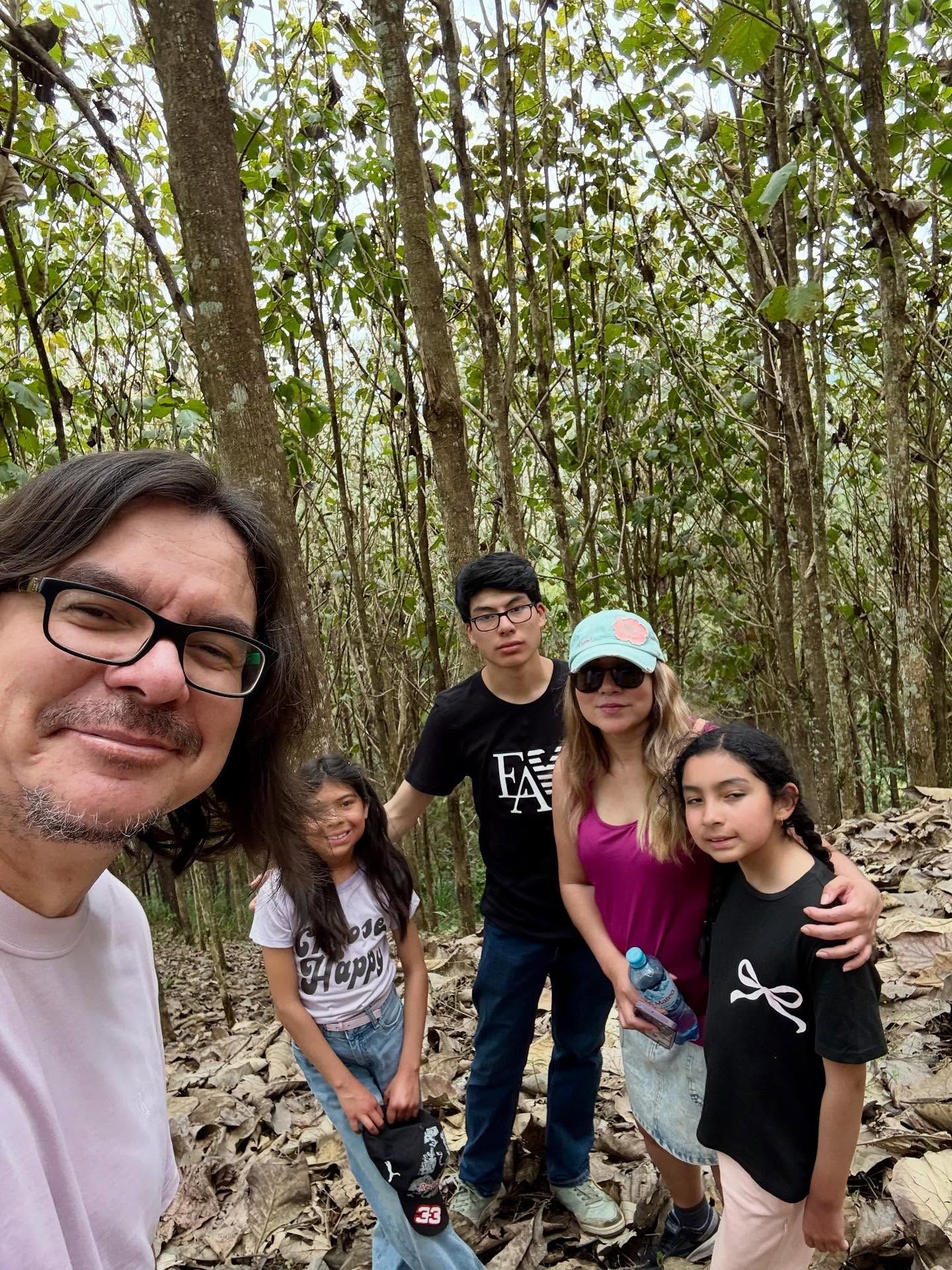 Grupo de cinco amigos sonrientes posando en un sendero forestal con árboles altos y vegetación.