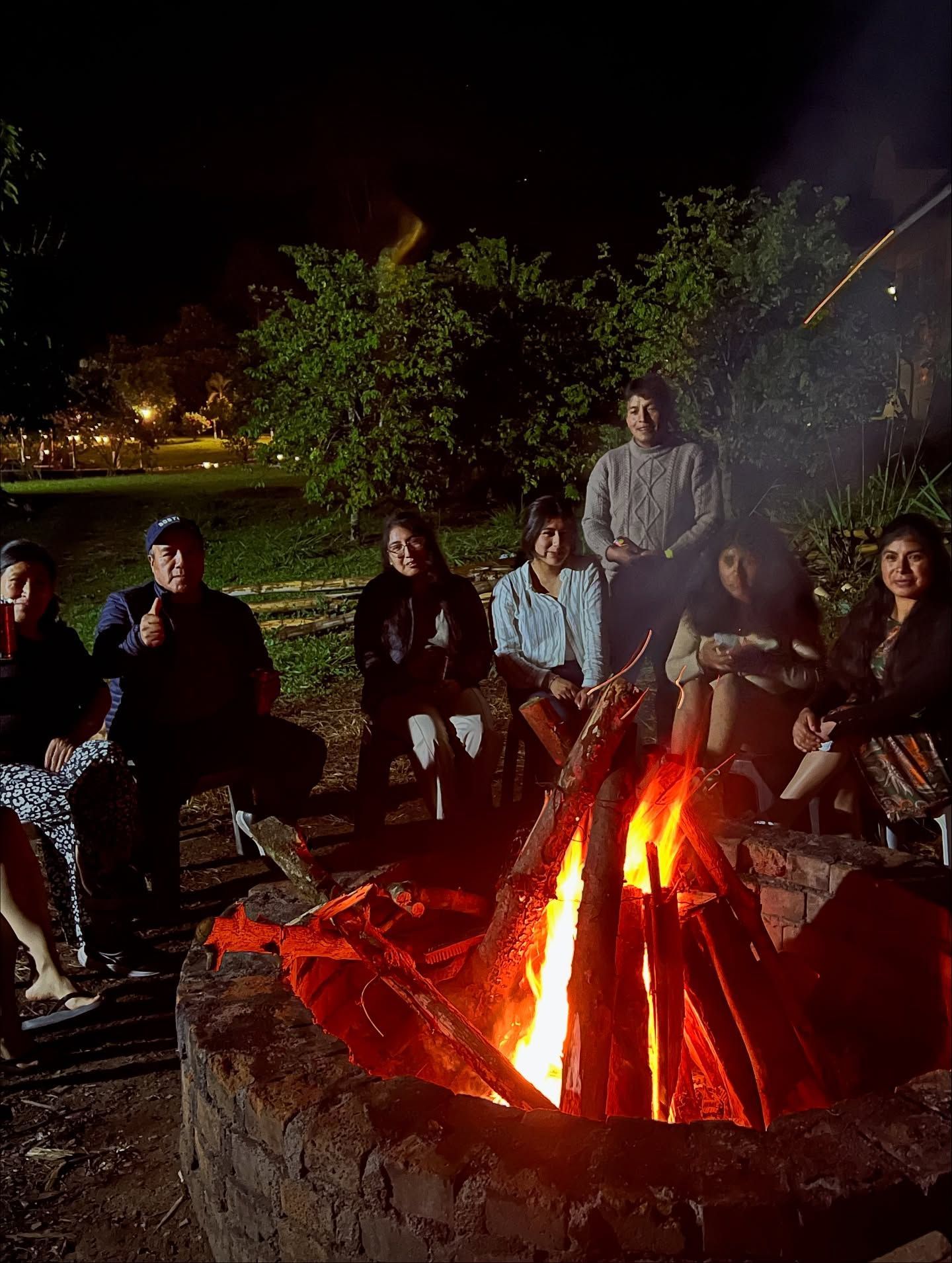 Personas sentadas alrededor de una fogata por la noche en un entorno boscoso al aire libre.