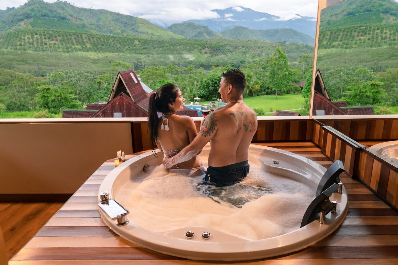 Una pareja se relaja en un jacuzzi en una terraza de madera con vistas a la montaña.
