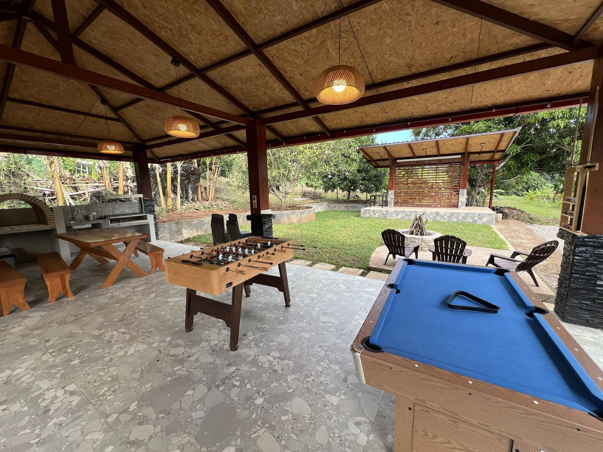 Patio al aire libre con mesa de billar, mesa de ajedrez y asientos con vistas a un jardín con césped.