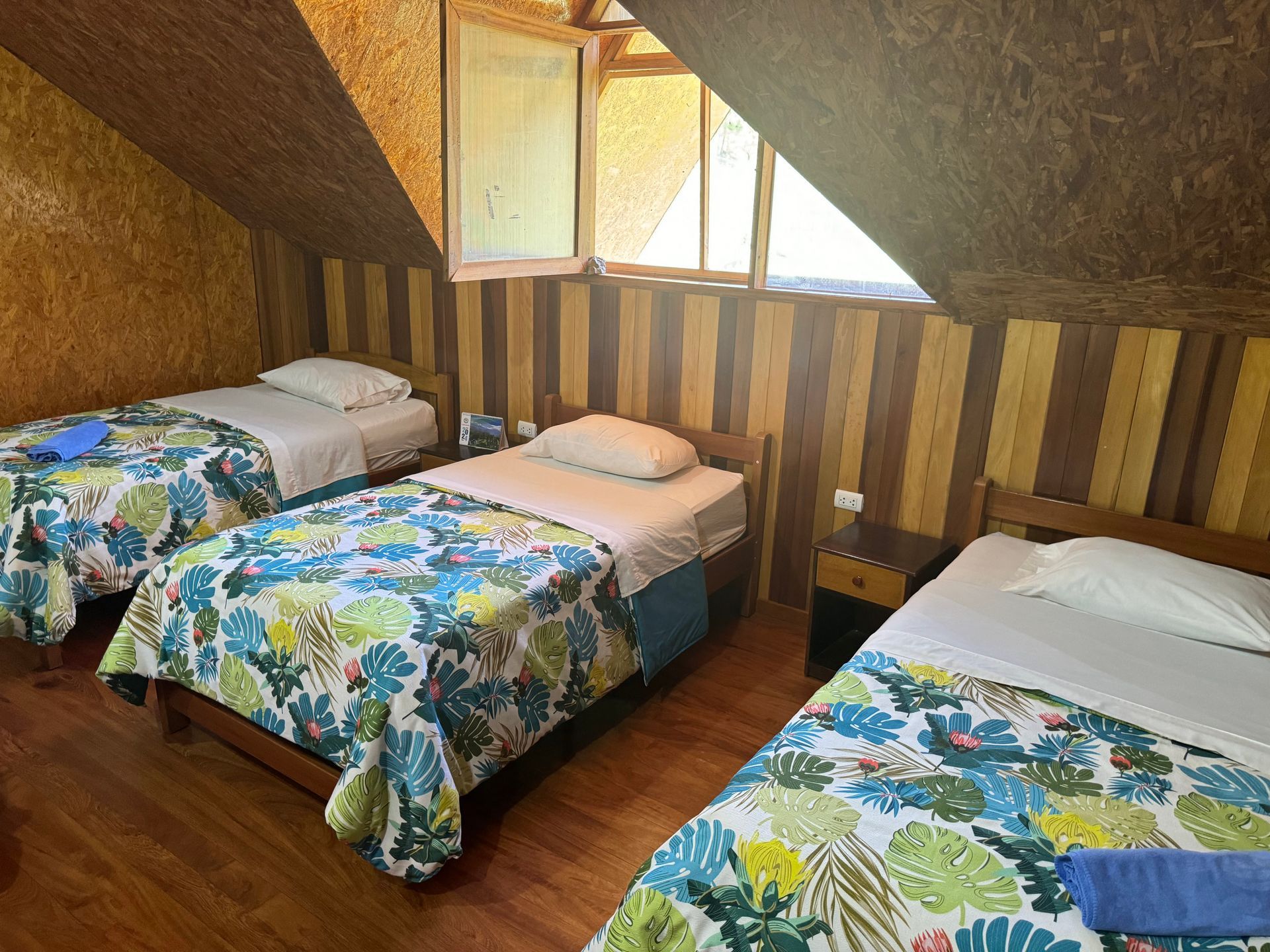 Tres camas individuales con mantas florales en un acogedor dormitorio abuhardillado con paneles de madera.