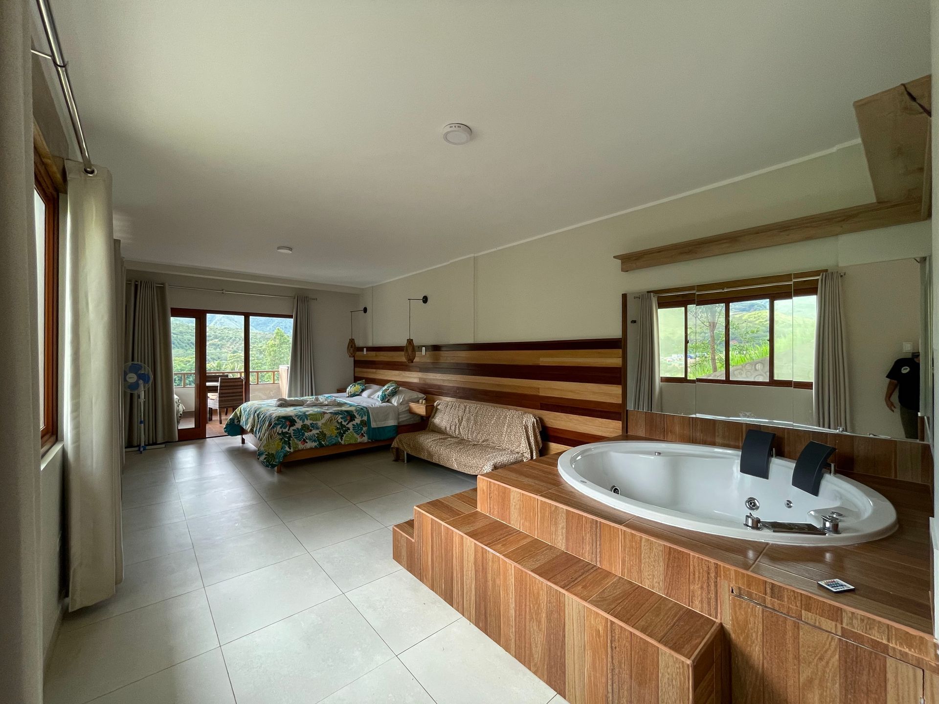 Habitación luminosa con una gran bañera de hidromasaje, cama, pared revestida de madera y puertas corredizas de vidrio que dan a un patio.