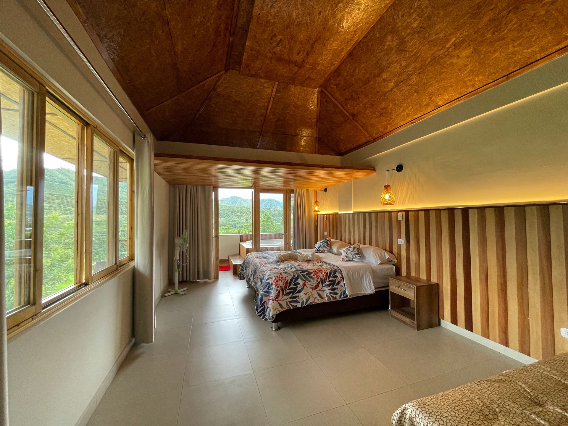 Acogedora habitación con techo abovedado de madera, grandes ventanales y una cama junto a una pared decorativa con rayas.