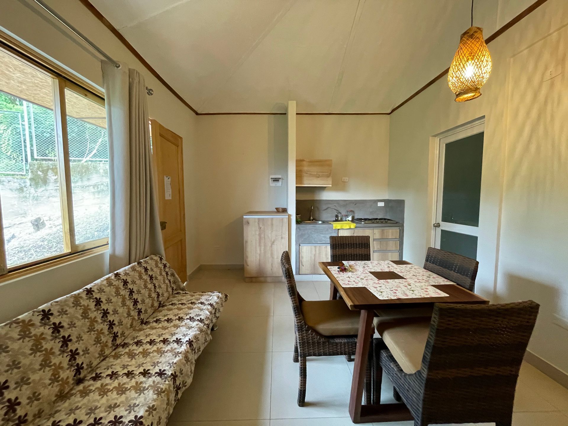Pequeño salón-comedor con sofá estampado, mesa de madera, sillas y rincón de cocina junto a la ventana.